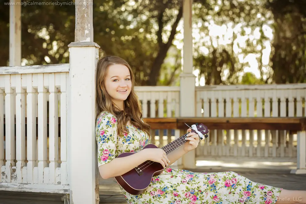 Senior girl sitting with her ukulele against a gazebo post in Downtown Mesa.