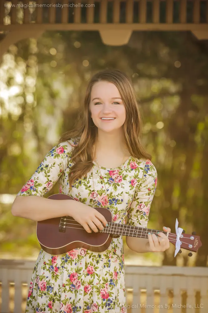 Senior girl in a floral dress holding a ukulele during her photo session at the Sirrine House gazebo in Downtown Mesa.