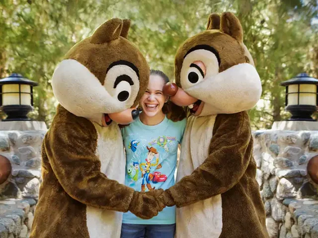 Girl smiling between Chip and Dale while holding hands with both characters at Disneyland.